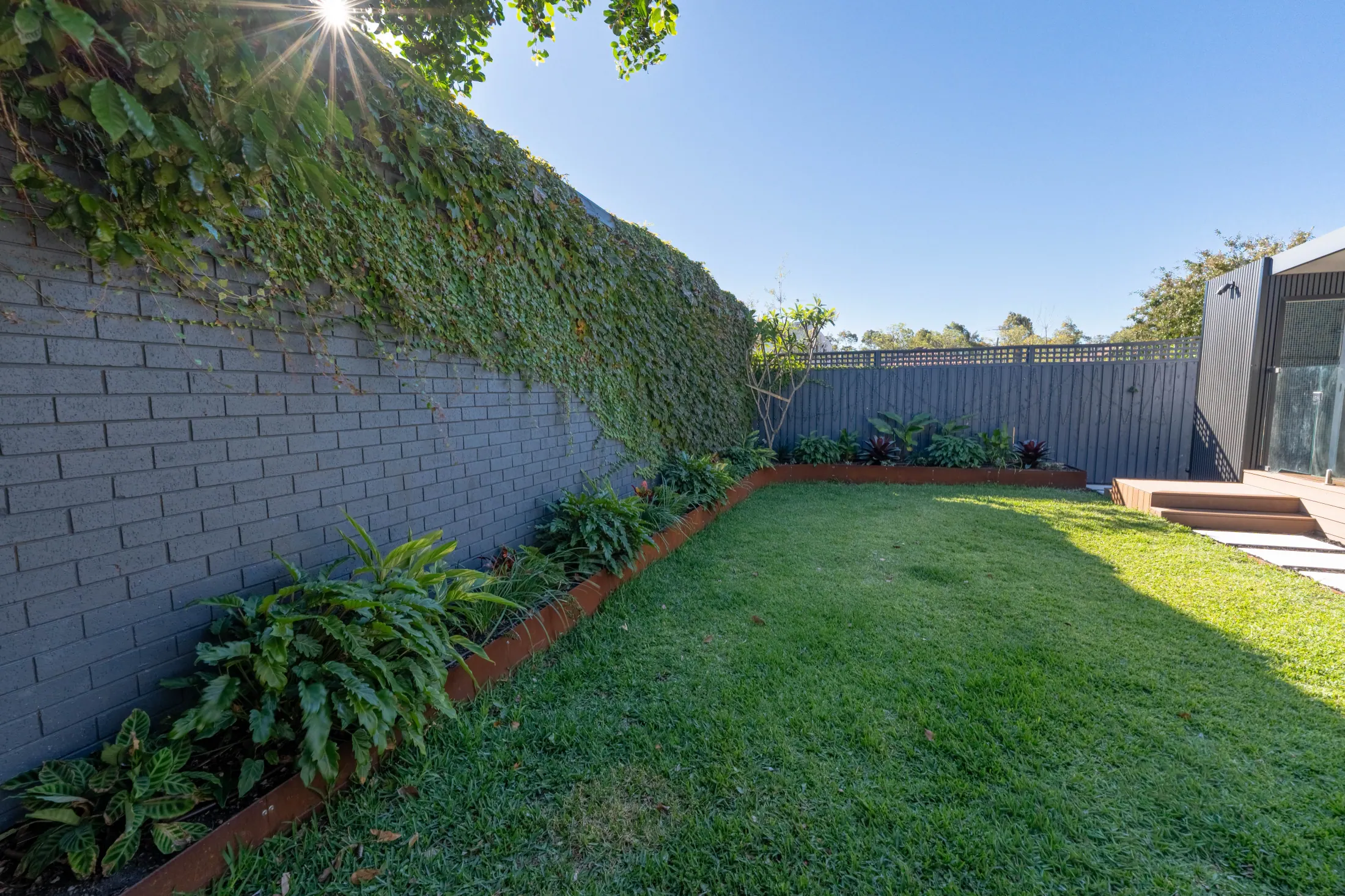 Established garden beds and lawn maturing along a rendered wall