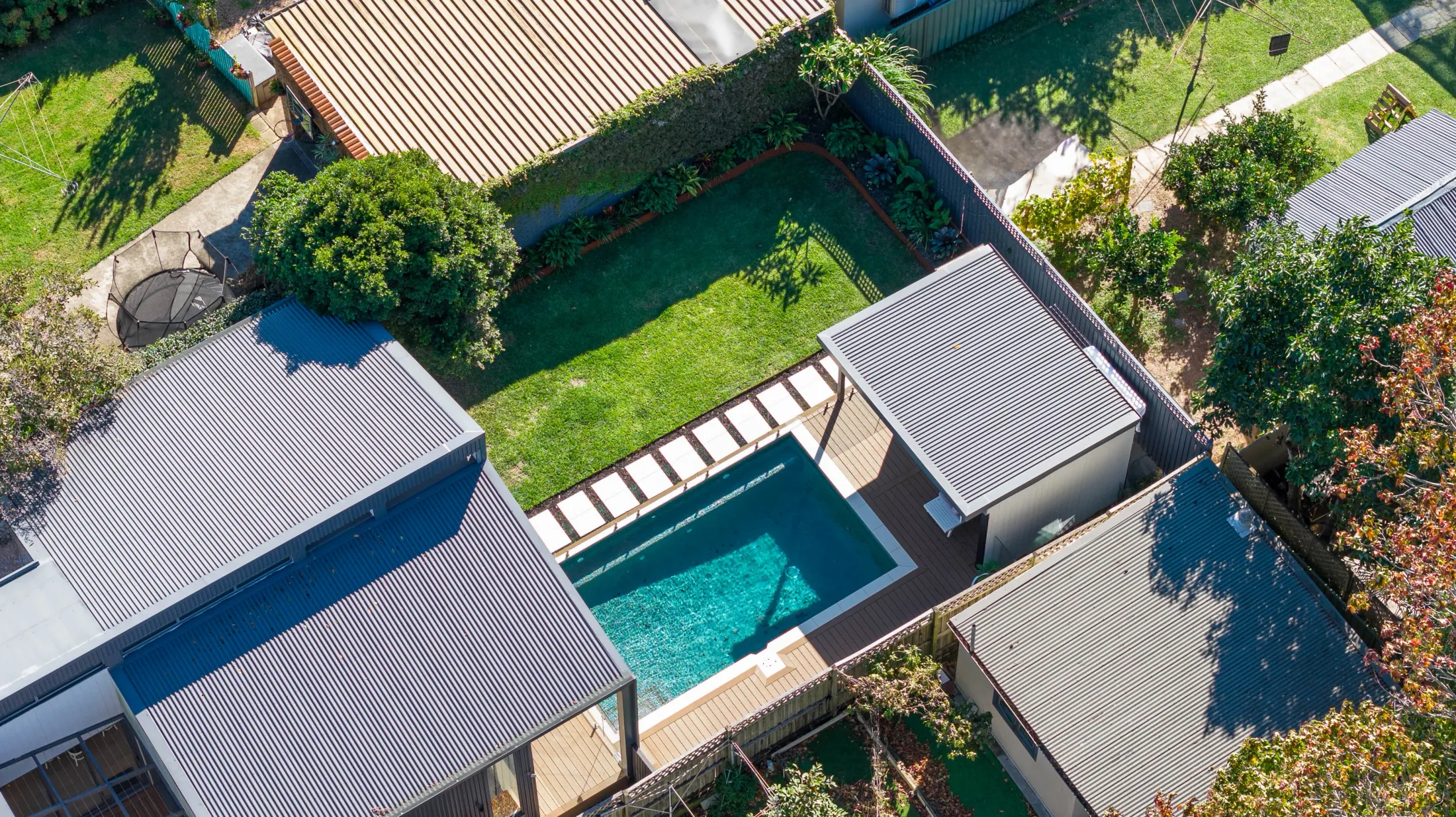 A landscaped backyard in Earlwood — lawn and garden beds, timber deck and paved terrace